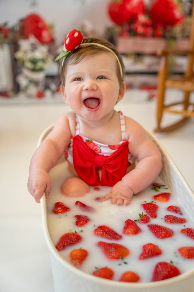 Infant in a strawberry milk bath smiling at the camera. Great idea inspiration for themed photoshoots.