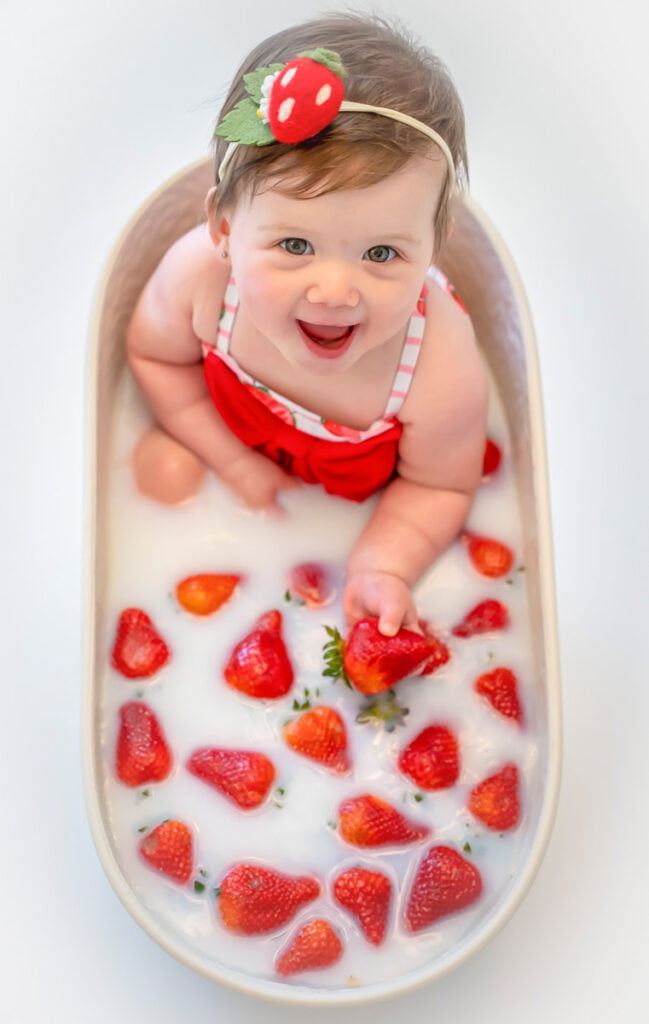 Cute baby toddler in a milk bath with strawberries for spring and summer themed photoshoot